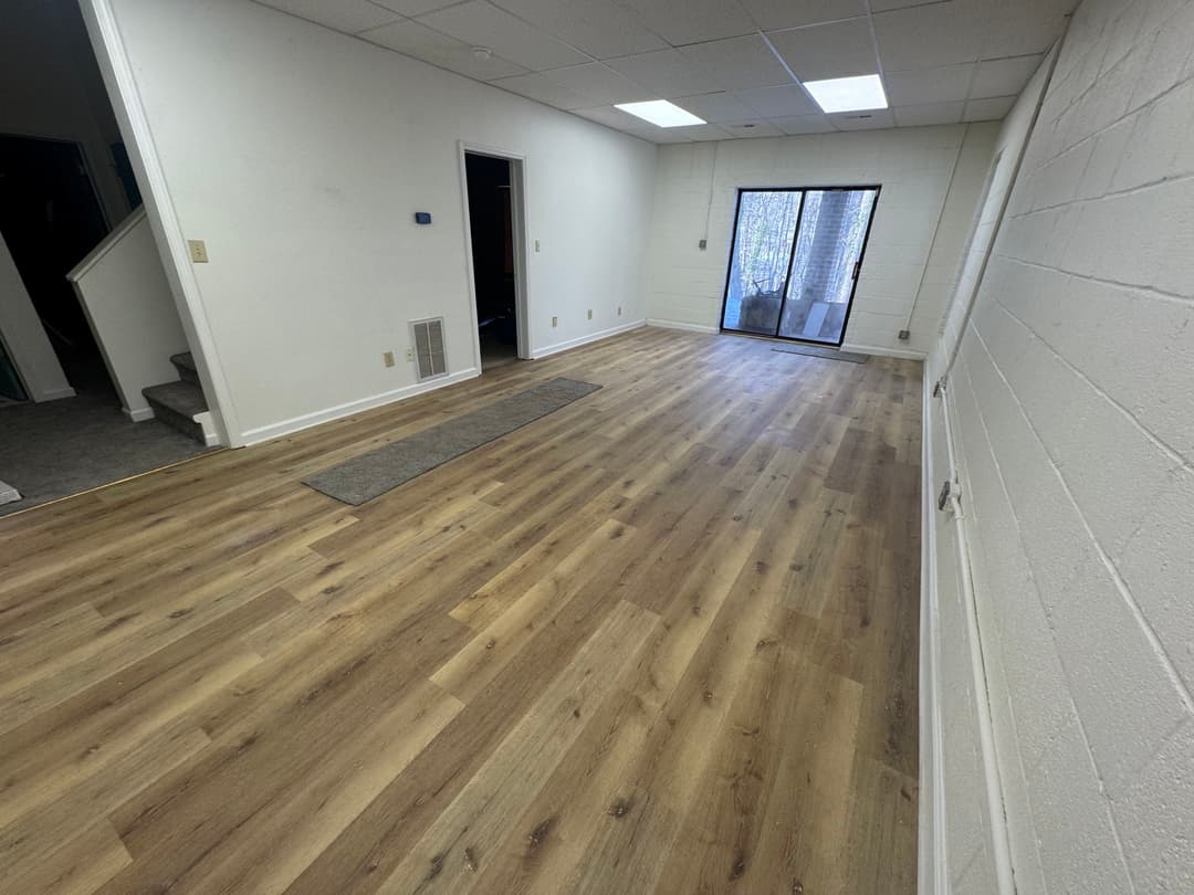 Spacious empty room with wood flooring and sliding glass door leading to outdoor area.