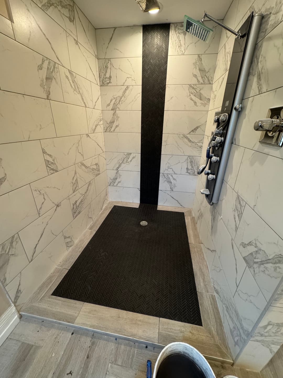 Modern shower renovation with marble tiles and a textured black floor.