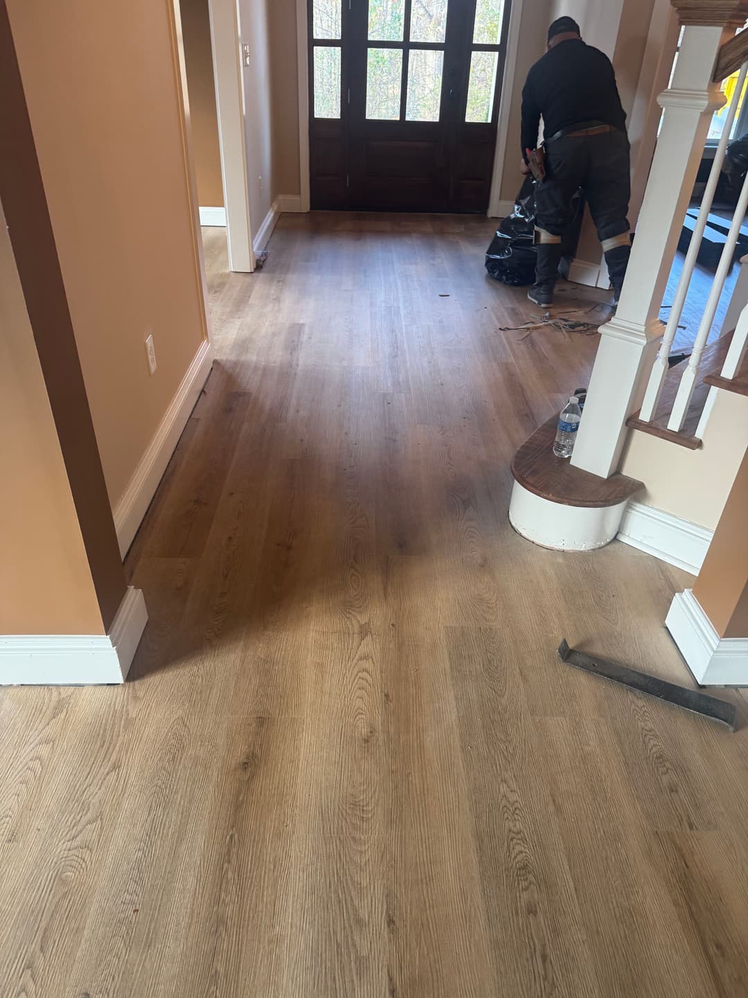 Wooden flooring installation underway in a home entrance with a worker and staircase.