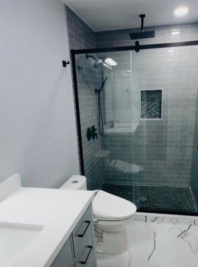 Modern bathroom with gray tile shower, glass door, and sleek white vanity.