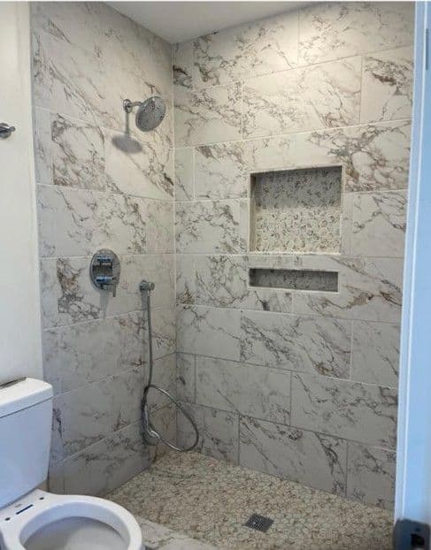Modern bathroom featuring a marble-tiled shower and recessed niche, with a toilet nearby.